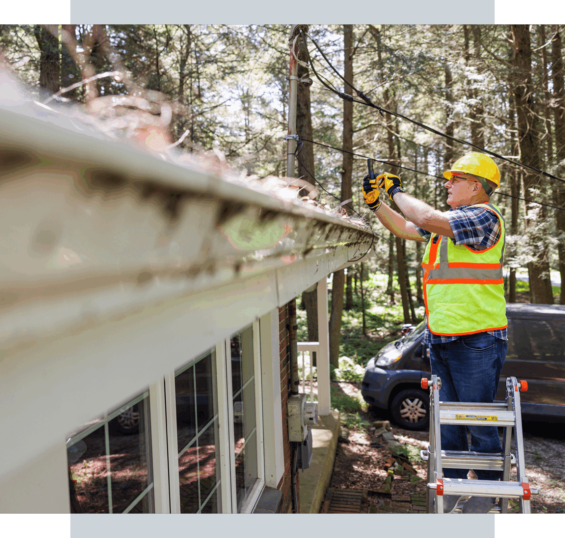 Worker cleaning gutters on a ladder.