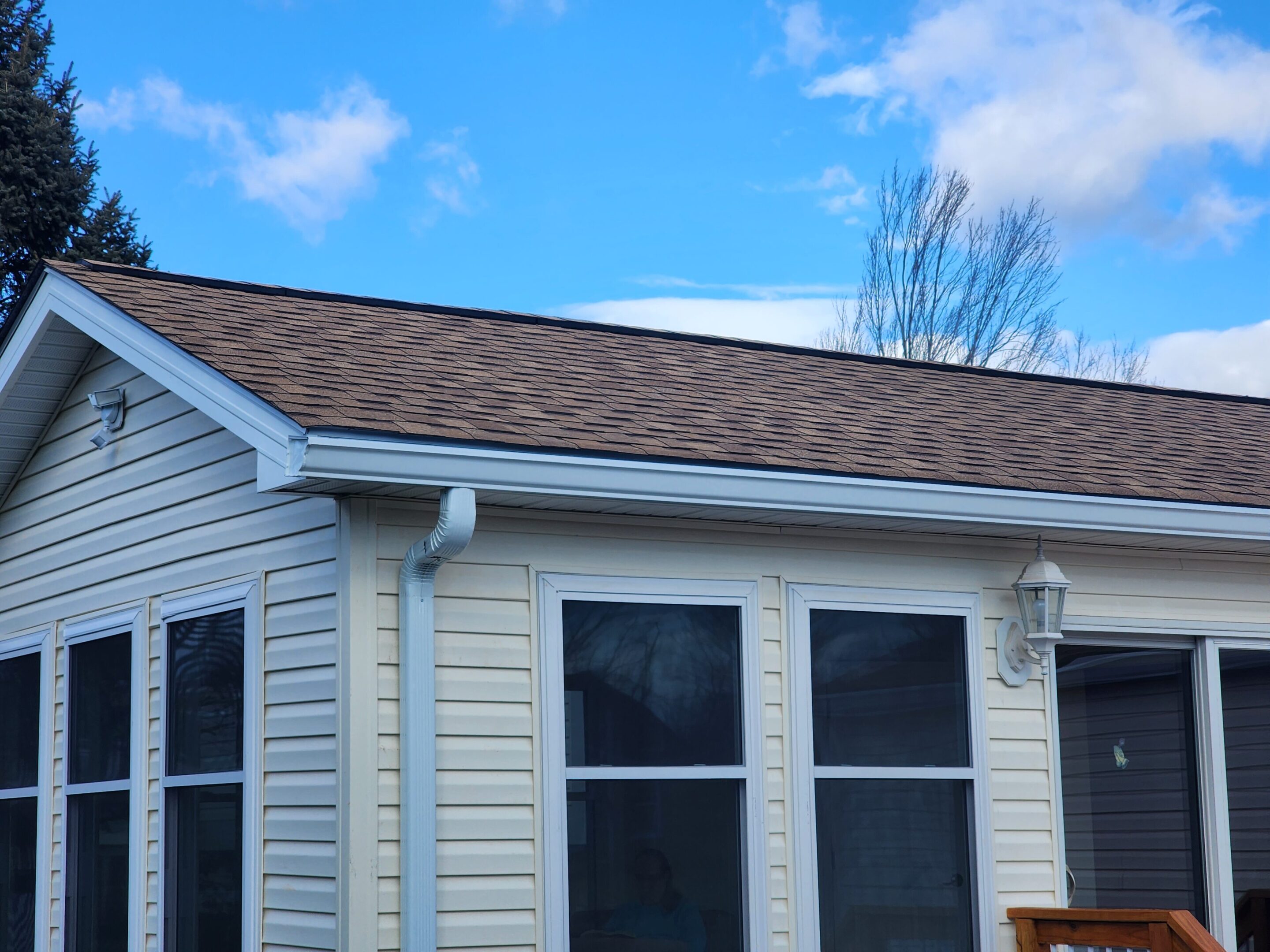 A house exterior with beige siding and a brown shingled roof under a clear blue sky.